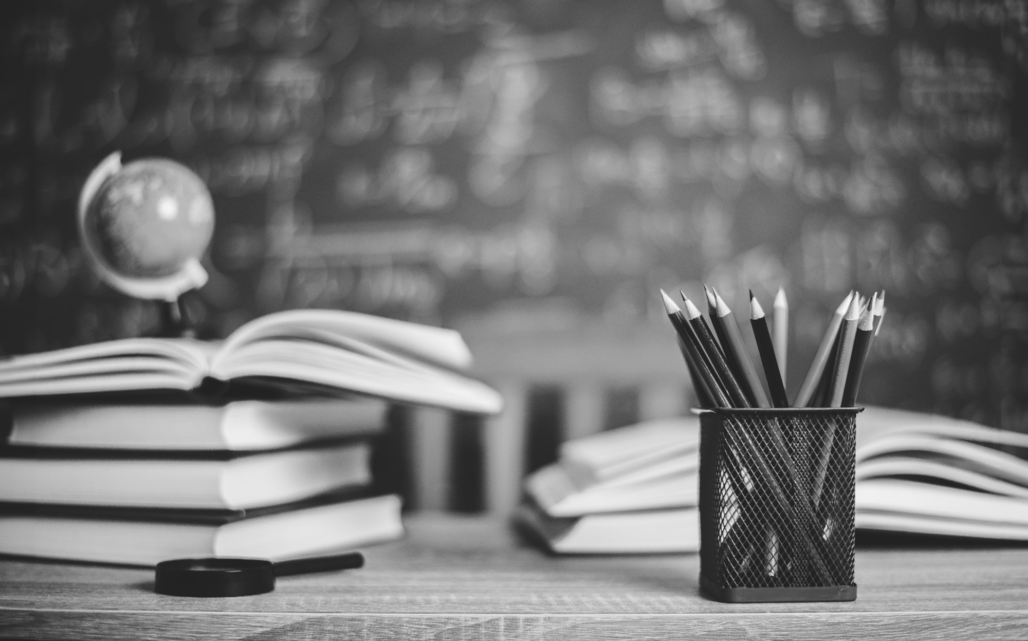 Black and white image of a study area at a Hackney tuition centre, featuring open books, a globe, a magnifying glass, and a pencil holder.