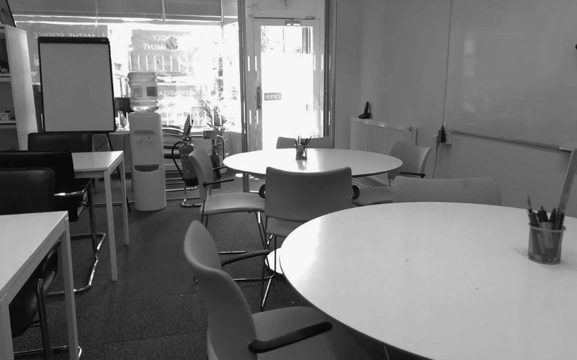 Interior of Hackney Tuition Centre with round tables, chairs, a whiteboard, and a water dispenser, set up for a contact tutoring session.